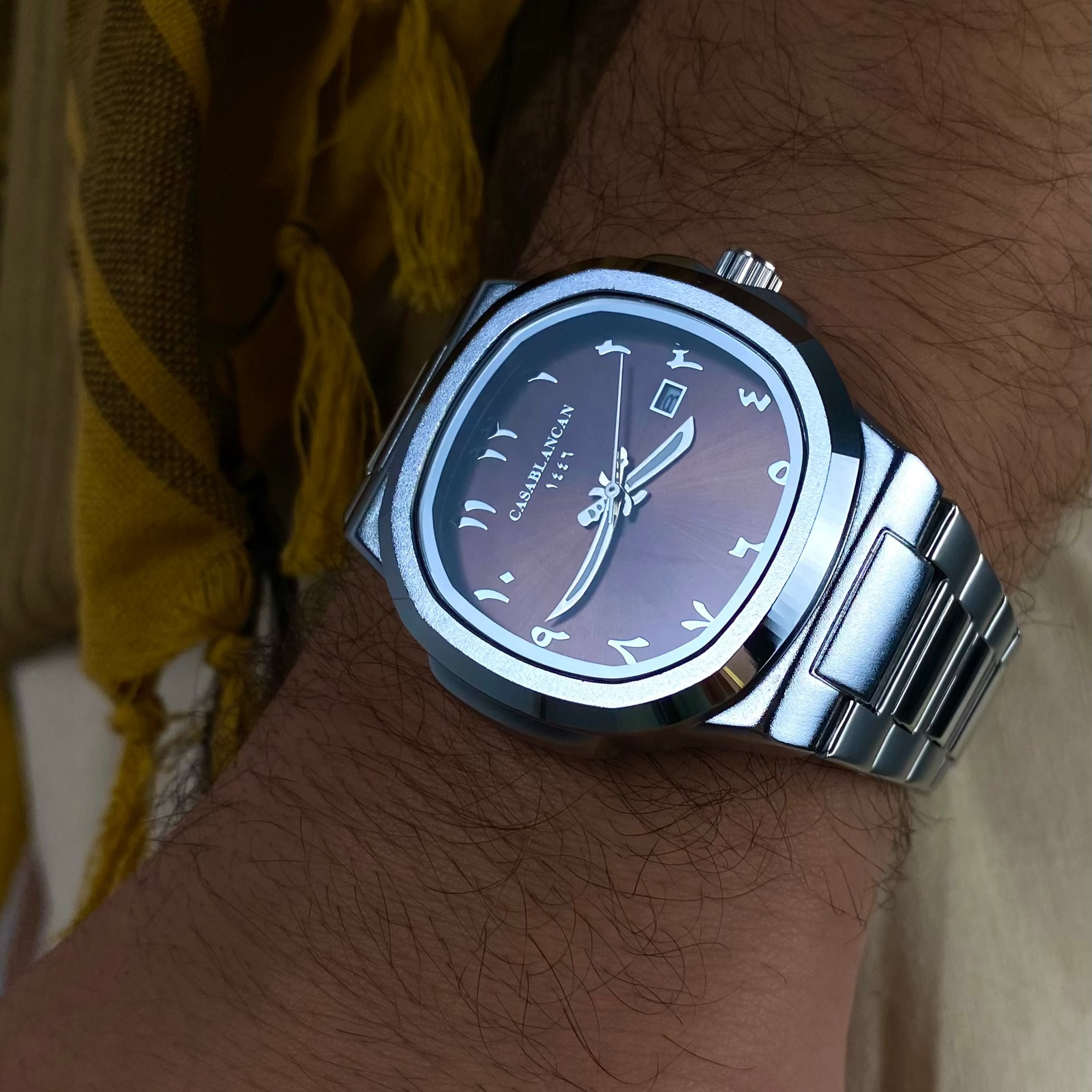 model's Wrist wearing Casablancan Dune Heritage Arabic numerals brown dial 43mm Watch, against a yellow fabric background.